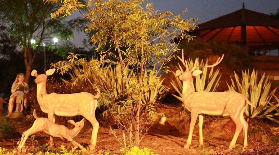 Illuminated life-sized deer statues in the park at Nrupatunga Betta, Hubli, at night.